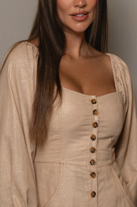 Woman wearing a beige dress with buttons and a matching cardigan against a neutral background