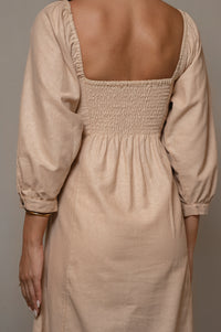 Beige dress with smocked back and long sleeves on a neutral background