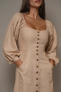 Woman wearing a beige dress with button details against a neutral background