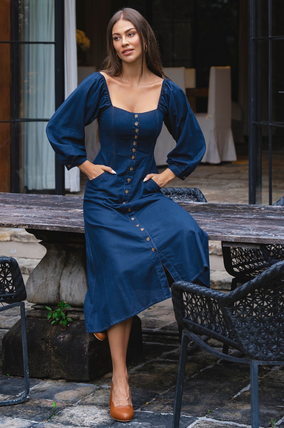 Woman in a blue dress standing outdoors on a patio.