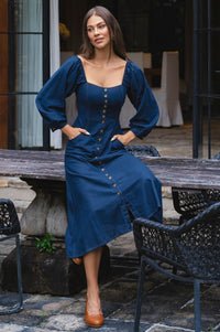 Woman in a blue dress standing outdoors on a patio.