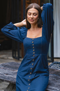 Woman wearing a blue dress with buttons, standing outdoors.