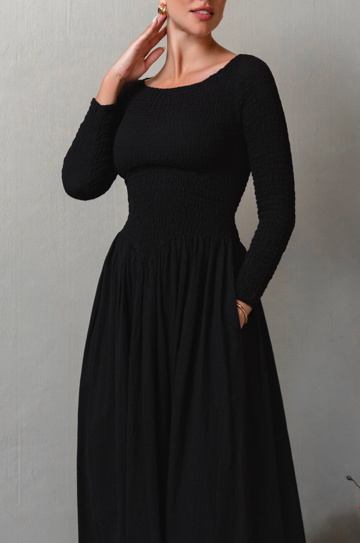 Woman wearing a black long-sleeve smocked dress against a plain background