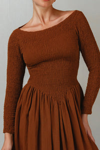 Brown smocked dress with long sleeves on a neutral background
