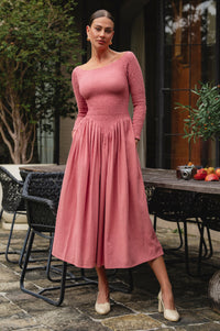 Woman in a pink smocked dress standing outdoors near a table with fruit.