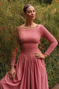 Woman wearing a pink linen dress standing against a green foliage background