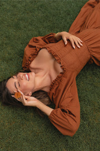 Woman in a rust-colored midi dress lying on a grass