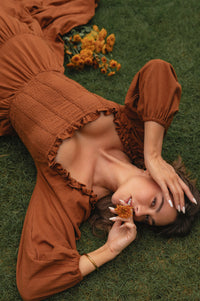 Woman in a brown outfit lying on grass with flowers around her country style