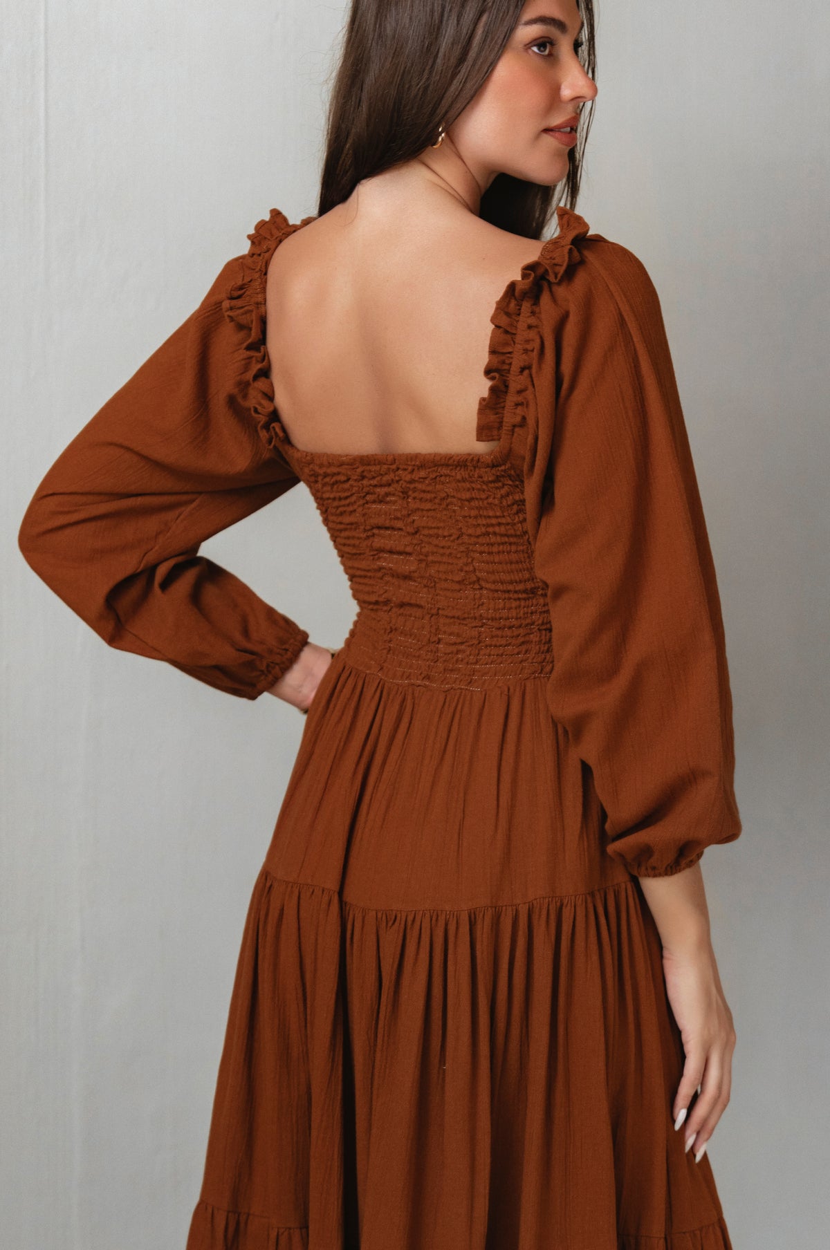 Brown dress with long sleeves and ruffled details on a plain background