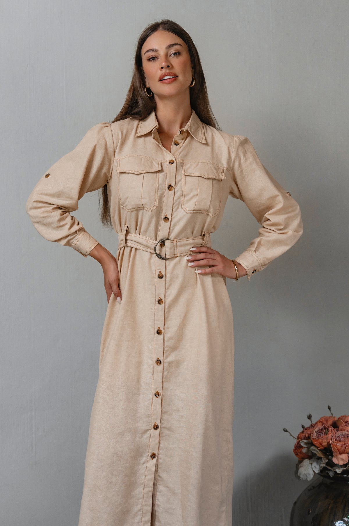 Woman wearing a beige dress with a belt against a gray background