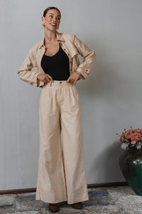 Woman wearing a beige jacket and pants with a black top, standing against a plain wall -cottage core style