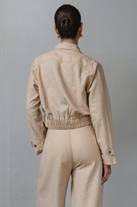 Person wearing a beige jacket and pants against a gray background