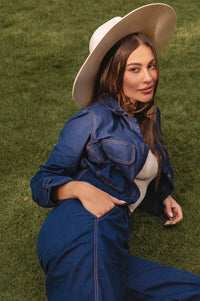 Woman wearing a blue denim outfit and white hat sitting on grass