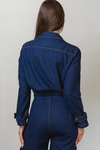 Person wearing a blue denim jacket and pants against a plain background