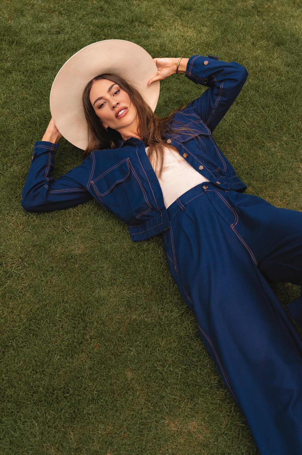 Woman in a blue outfit and beige hat lying on grass - cottage core style