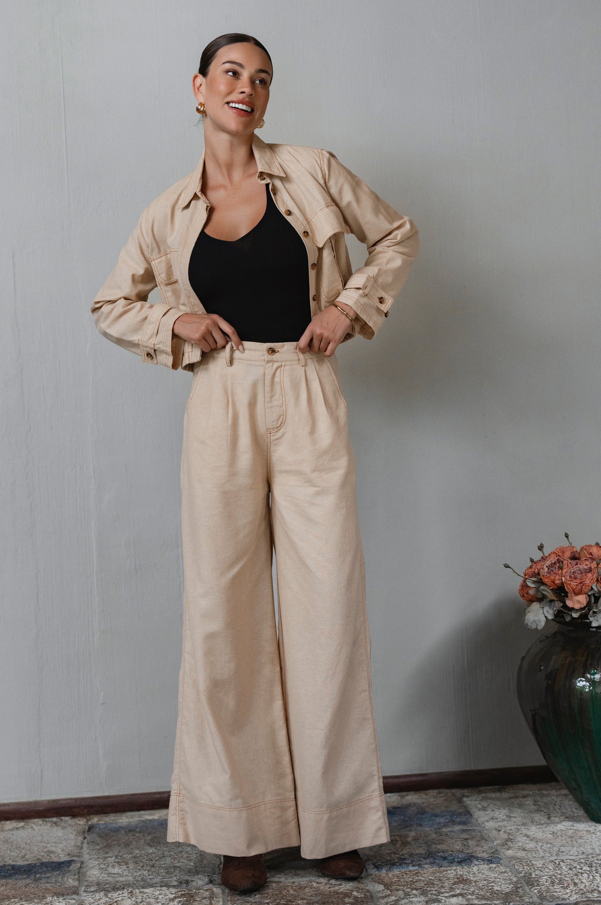 Woman wearing a beige jacket and pants with a black top, standing against a plain wall. - cottage core style