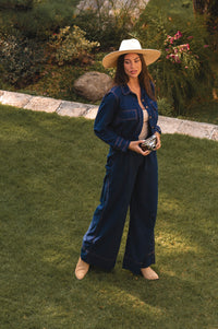 Woman in a blue set and white hat standing on grass with a garden background - cottage core style