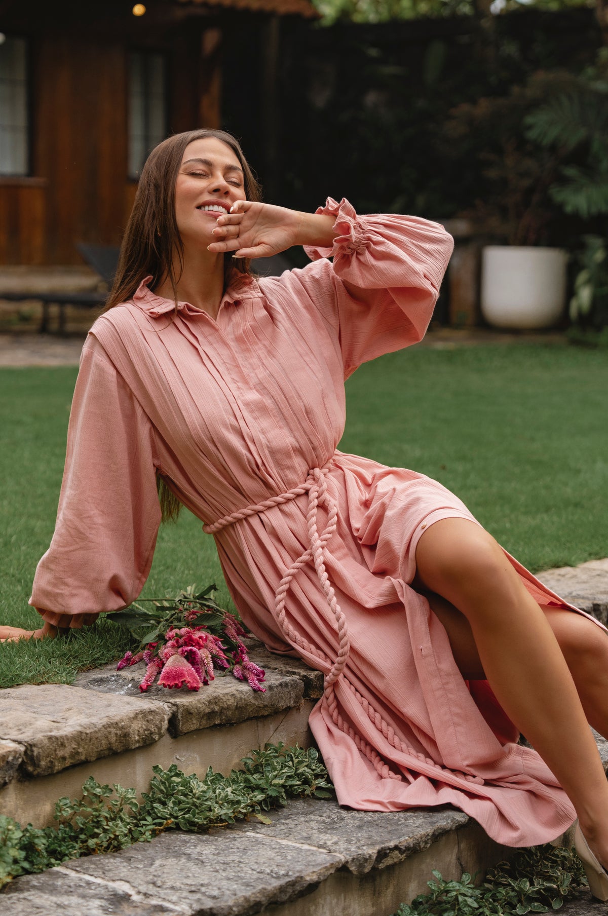 Woman in a pink long sleeve dress sitting on stone steps outdoors