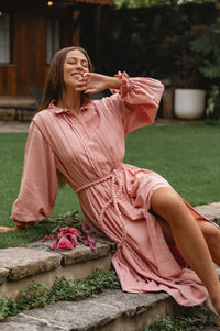 Woman in a pink long sleeve dress sitting on stone steps outdoors