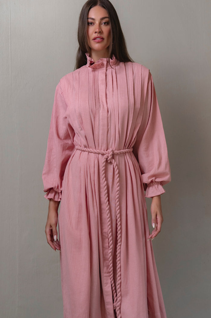 Woman wearing a pink dress with long sleeves against a gray background