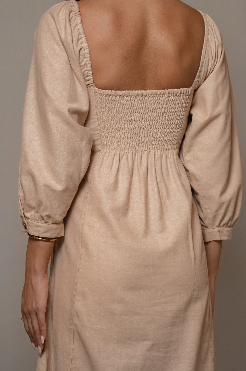 Beige dress with smocked back and long sleeves on a neutral background